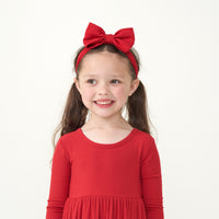 alternate image of a child wearing a Holiday Red ribbed twirl dress paired with a Holiday Red luxe bow headband