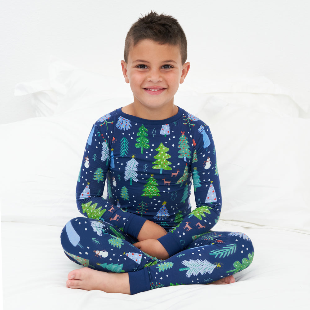 Child sitting on a bed wearing a Blue Merry and Bright two piece pajama set
