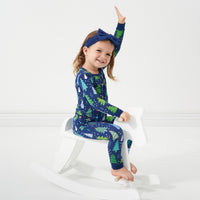 Child playing on a rocking horse wearing a Blue Merry and Bright two piece pajama set paired with a Sapphire Luxe Bow headband