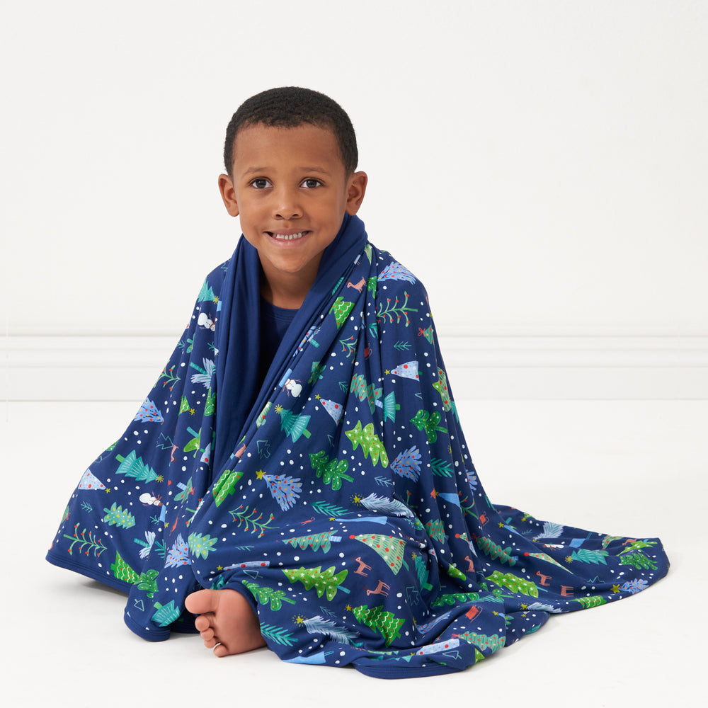Child sitting wrapped up in a Blue Merry and Bright cloud blanket
