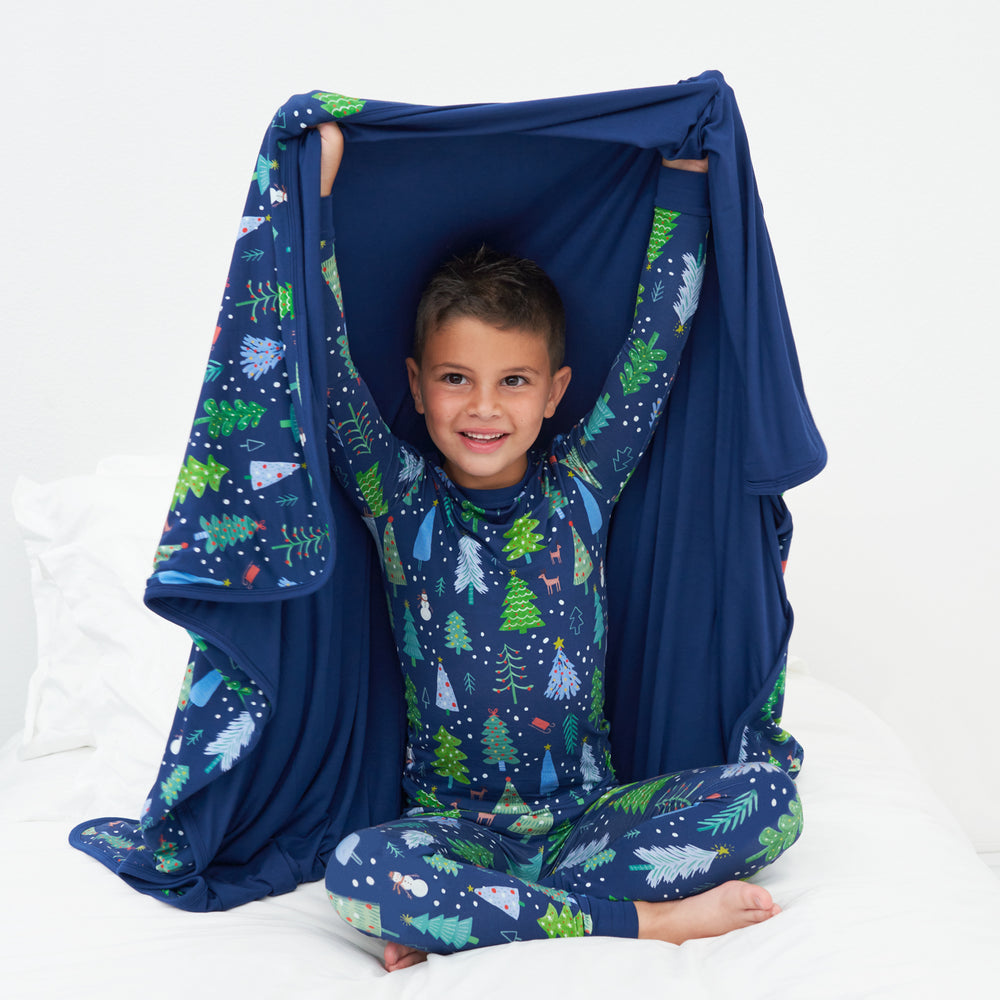 Child wearing a Blue Merry and Bright two piece pajama set hold up a matching Blue Merry and Bright cloud blanket showing off the solid Sapphire backing.