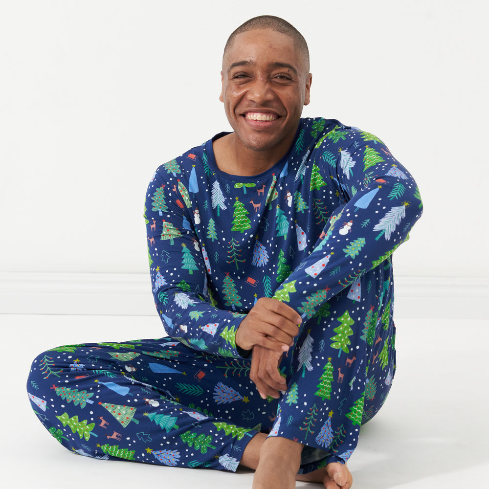 Man sitting wearing Blue Merry and Bright printed pajama bottoms and a matching men's Blue Merry and Bright pajama top