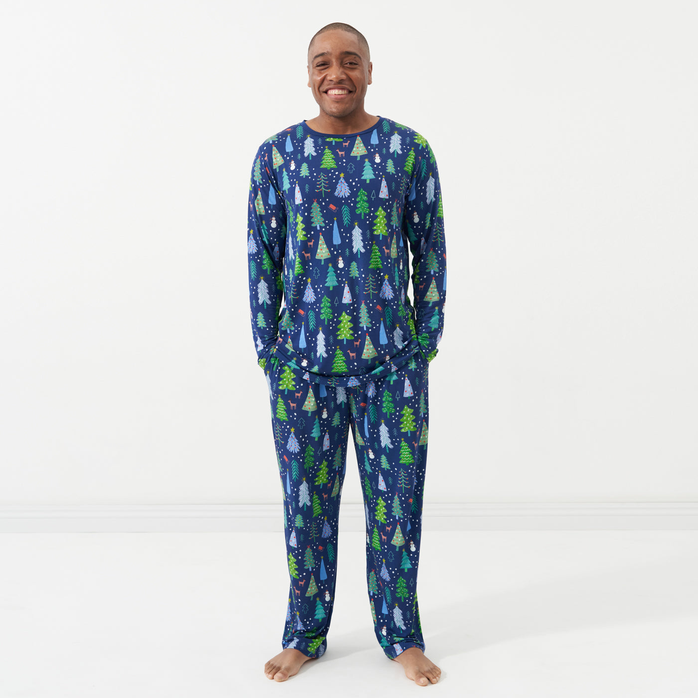 Man posing with his hands in his pockets wearing Blue Merry and Bright printed pajama bottoms and a matching men's Blue Merry and Bright pajama top