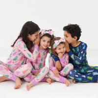 four children playing wearing coordinating Pink and Blue Merry and Bright two piece pajama sets. Two children paired their Pink Merry and Bright two piece pajama sets with matching luxe bow headbands