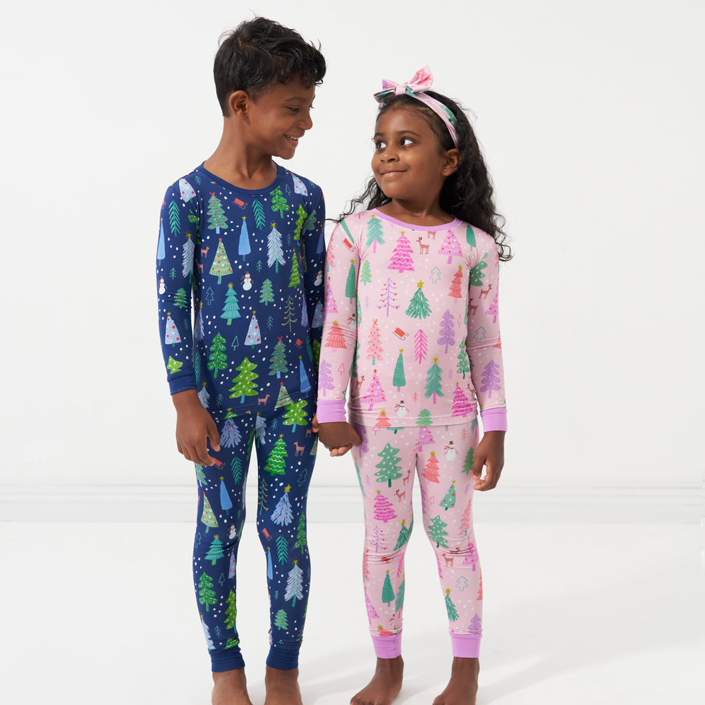 Two children holding hands wearing coordinating Pink and Blue Merry and Bright two piece pajama sets. The little girl has a her pjs paired with a matching Pink Merry and Bright luxe bow headband