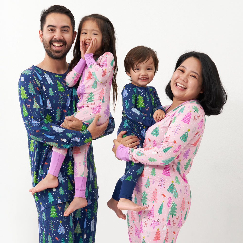Family of four wearing matching Merry and Bright pajamas. Dad is wearing Blue Merry and Bright men's pajama top and pajama bottoms. Mom is wearing Pink Merry and Bright women's pajama top and pajama bottoms. Children are wearing matching pink and blue Merry and Bright zippies
