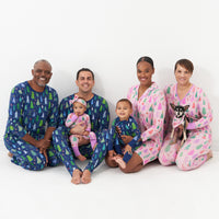 Family and their dog posing. Dad and Grandpa are wearing Men's Blue Merry and Bright men's pajama top paired with matching men's pajama bottoms. Grandma is wearing a women's Pink Merry and Bright women's pajama top paired with matching women's pajama bottoms. Mom is wearing a Pink Merry and Bright women's sleep shirt. Their dog is wearing a Pink Merry and Bright pet bandana and their children are wearing Blue and Pink Merry and Bright zippies paired with a matching Pink Merry and Bright luxe bow headband