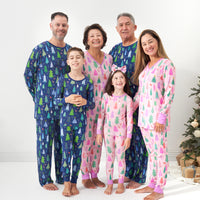 family of six wearing matching Merry and Bright pajamas. Dad and Grandpa are wearing Blue Merry and Bright printed men's pajama top and men's pajama bottoms. Mom and Grandma are wearing Pink Merry and Bright women's pajama top  and pajama bottoms. Children are wearing Blue and Pink Merry and Bright two piece pajama sets. Their daughter is pairing her Pink Merry and Bright Pajama set with a matching luxe bow headband.