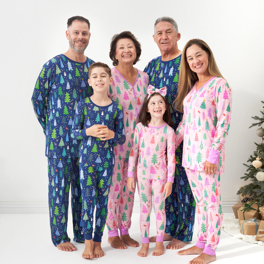 family of six wearing matching Merry and Bright pajamas. Dad and Grandpa are wearing Blue Merry and Bright printed men's pajama top and men's pajama bottoms. Mom and Grandma are wearing Pink Merry and Bright women's pajama top and pajama bottoms. Children are wearing Blue and Pink Merry and Bright two piece pajama sets. Their daughter is pairing her Pink Merry and Bright Pajama set with a matching luxe bow headband.