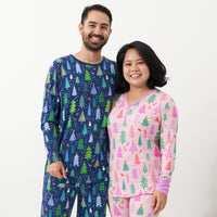 Close up image of a couple posing together wearing coordinating Merry and Bright pajamas. Man is wearing Blue Merry and Bright printed pajama bottoms and a matching men's Blue Merry and Bright pajama top. Woman is wearing Pink Merry and Bright printed pajama top paired with matching women's Pink Merry and Bright printed pajama bottoms.