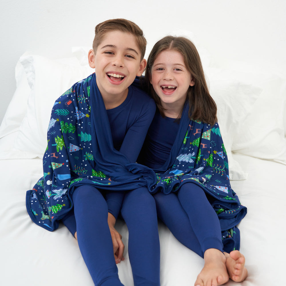 Two children cuddling under a Blue Merry and Bright cloud blanket wearing matching Sapphire two piece pajama sets