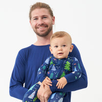 Father holding his son. Dad is wearing a men's Sapphire pajama top and his son is wearing a coordinating Blue Merry and Bright zippy