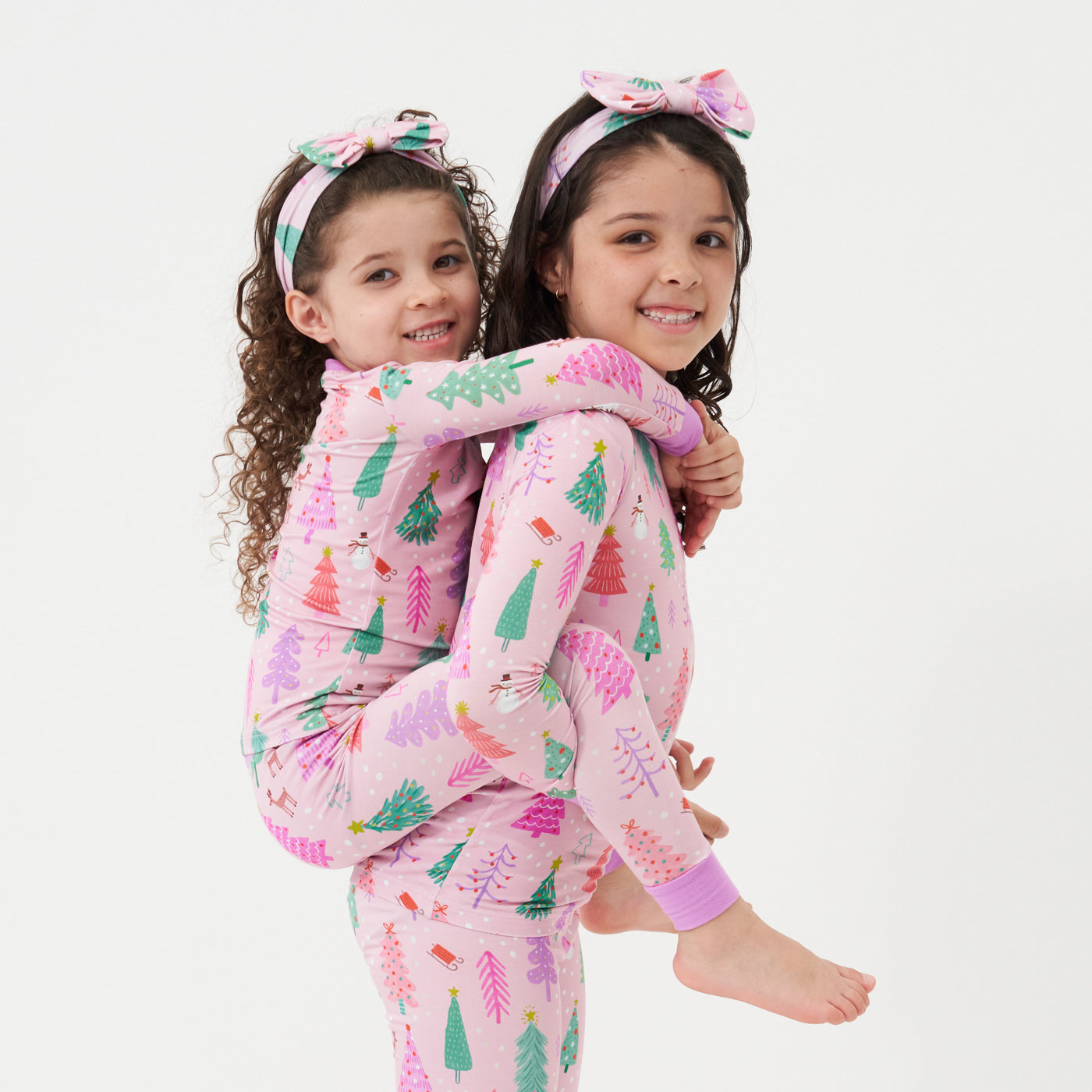 two children posing together wearing matching Pink Merry and Bright two piece paired with matching luxe bow headbands