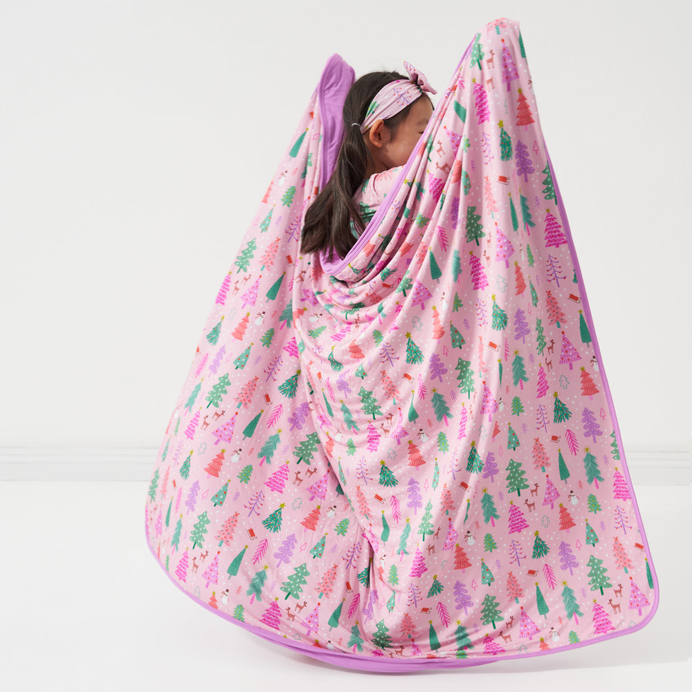 Back view of a child wearing a Pink Merry and Bright cloud blanket around her shoulders paired with a matching Pink Merry and Bright luxe bow headband