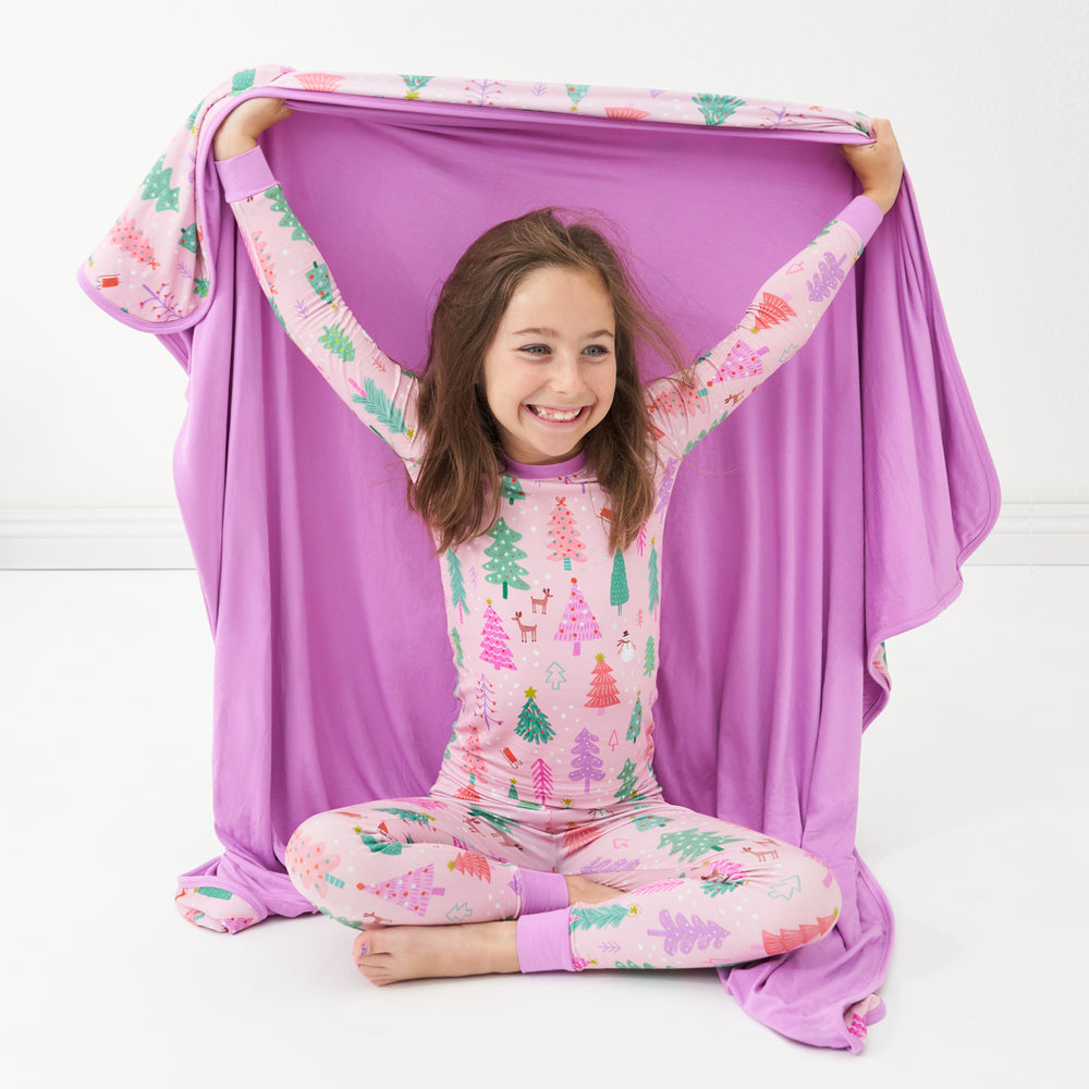 Child wearing a Pink Merry and Bright two piece pajama set hold up a matching Pink Merry and Bright cloud blanket showing off the solid Pink backing.