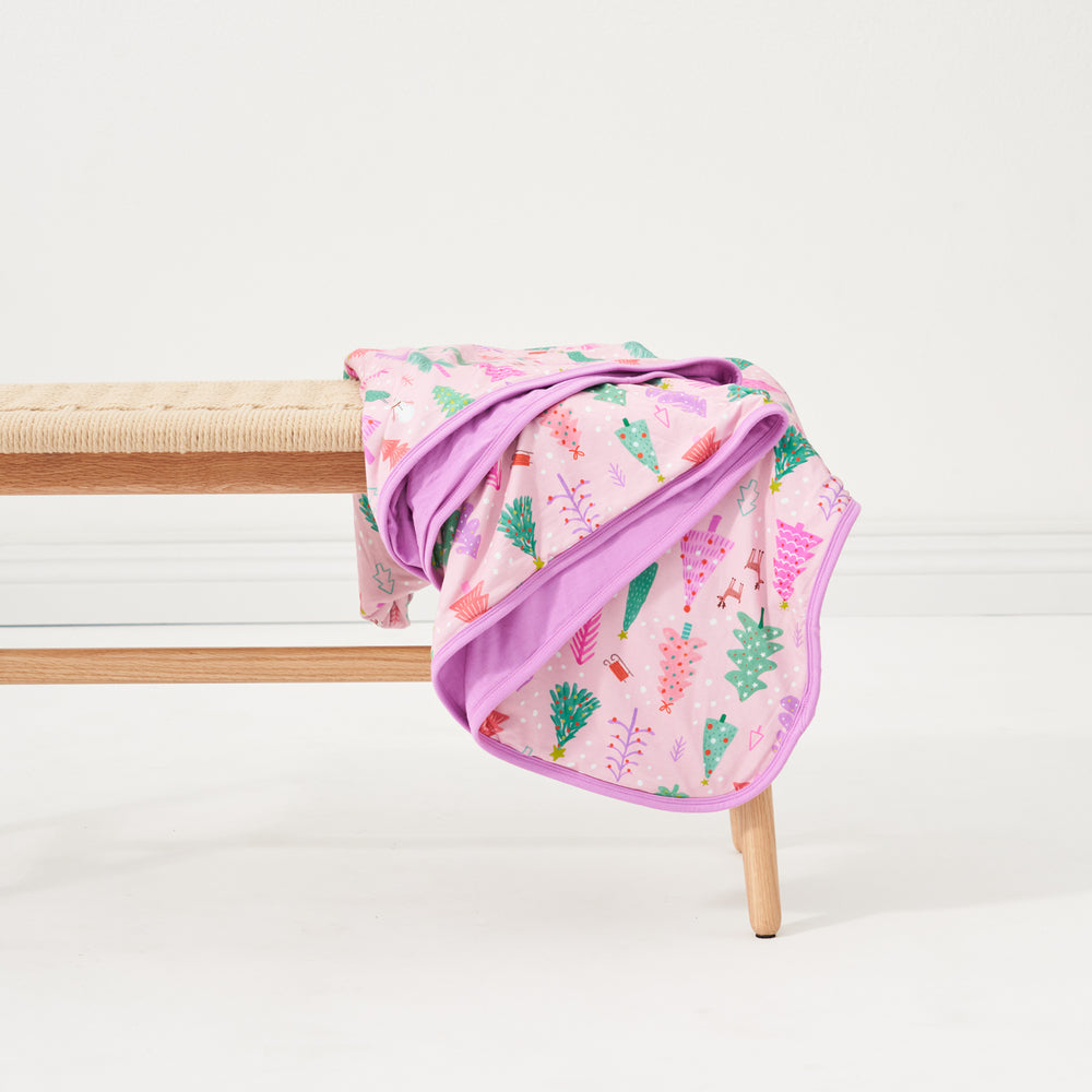 Image of a Pink Merry and Bright cloud blanket draped over the side of a bench