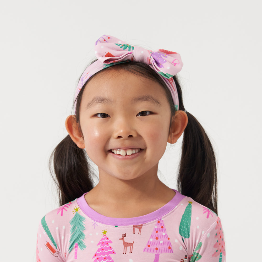 Close up image of a child wearing a Pink Merry and Bright two piece pajama set paired with a matching Pink Merry and Bright luxe bow headband in size age 4 to age 8