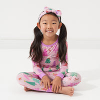Child wearing a Pink Merry and Bright two piece pajama set paired with a matching Pink Merry and Bright luxe bow headband in size age 4 to age 8