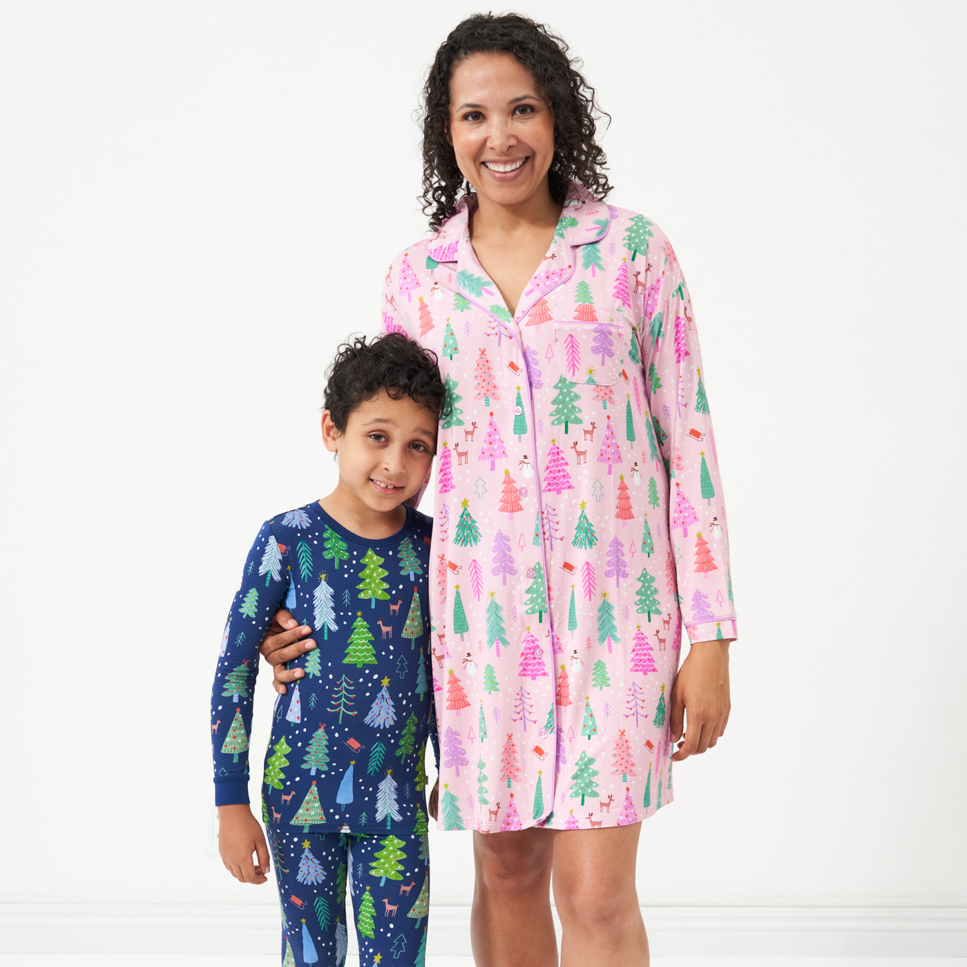 Woman wearing a Pink Merry and Bright women's sleep shirt holding her son's hand. Her son is wearing a coordinating Blue Merry and Bright two piece pajama set