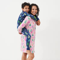 Woman wearing a Pink Merry and Bright women's sleep shirt holding her son on her back. Her son is wearing a coordinating Blue Merry and Bright two piece pajama set