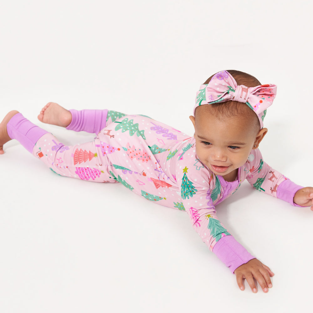 Child laying on a bed wearing a Pink Merry and Bright zippy paired with a matching Pink Merry and Bright luxe bow headband