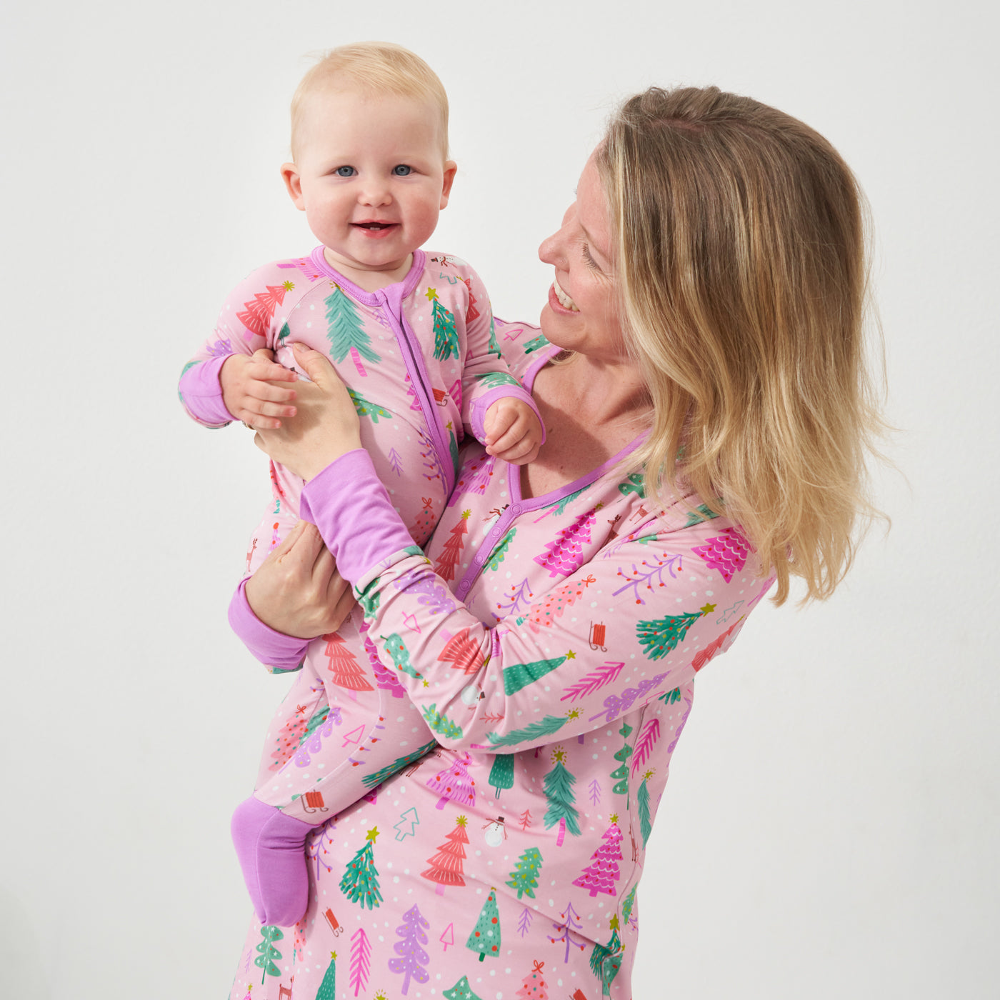 Mother holding her daughter wearing a Pink Merry and Bright printed women's pajama top and matching bottoms. Her daughter is wearing a Pink Merry and Bright zippy
