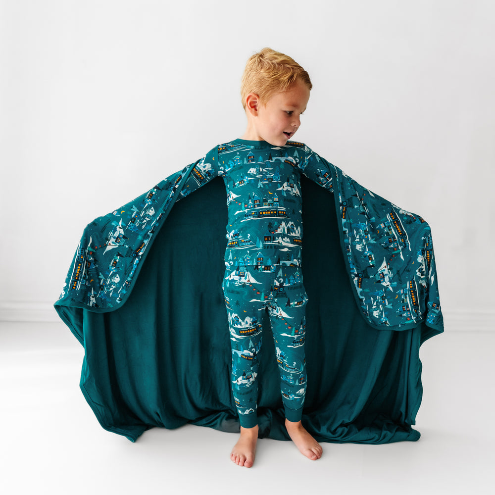 Child holding out a Midnight Express printed cloud blanket showing the solid teal backing. He is wearing matching Midnight Express printed two piece pajama set