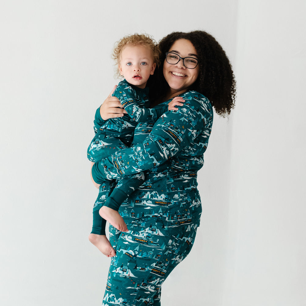 Mom holding her child wearing matching Midnight Express pajamas. Mom is wearing Midnight Express women's pajama pants paired with women's pajama top and child is wearing a matching printed zippy
