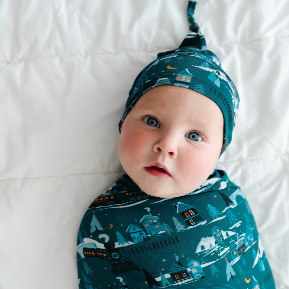 Close up image of a child laying on a bed swaddled in a Midnight Express swaddle and hat set