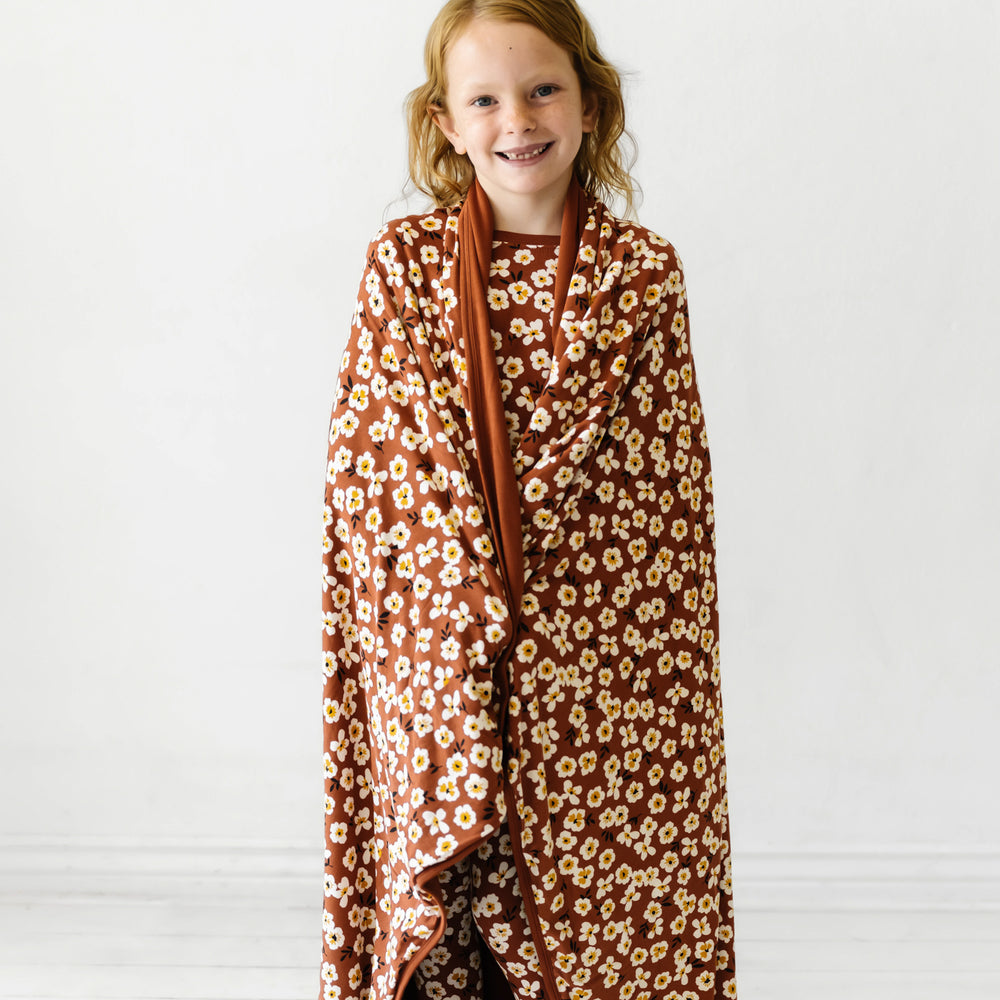 Child with a Mocha Blossom printed cloud blanket wrapped around their shoulders