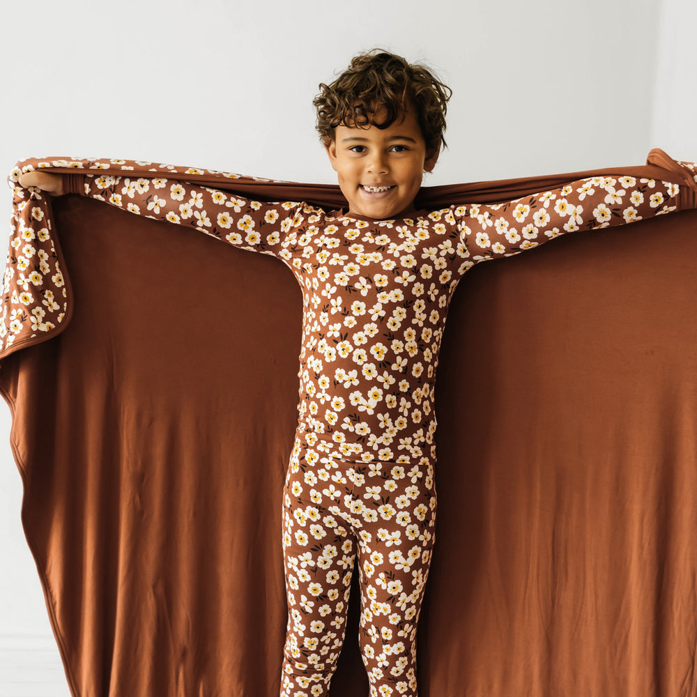 Child holding out a Mocha Blossom printed cloud blanket behind their shoulders showing the solid colored backing