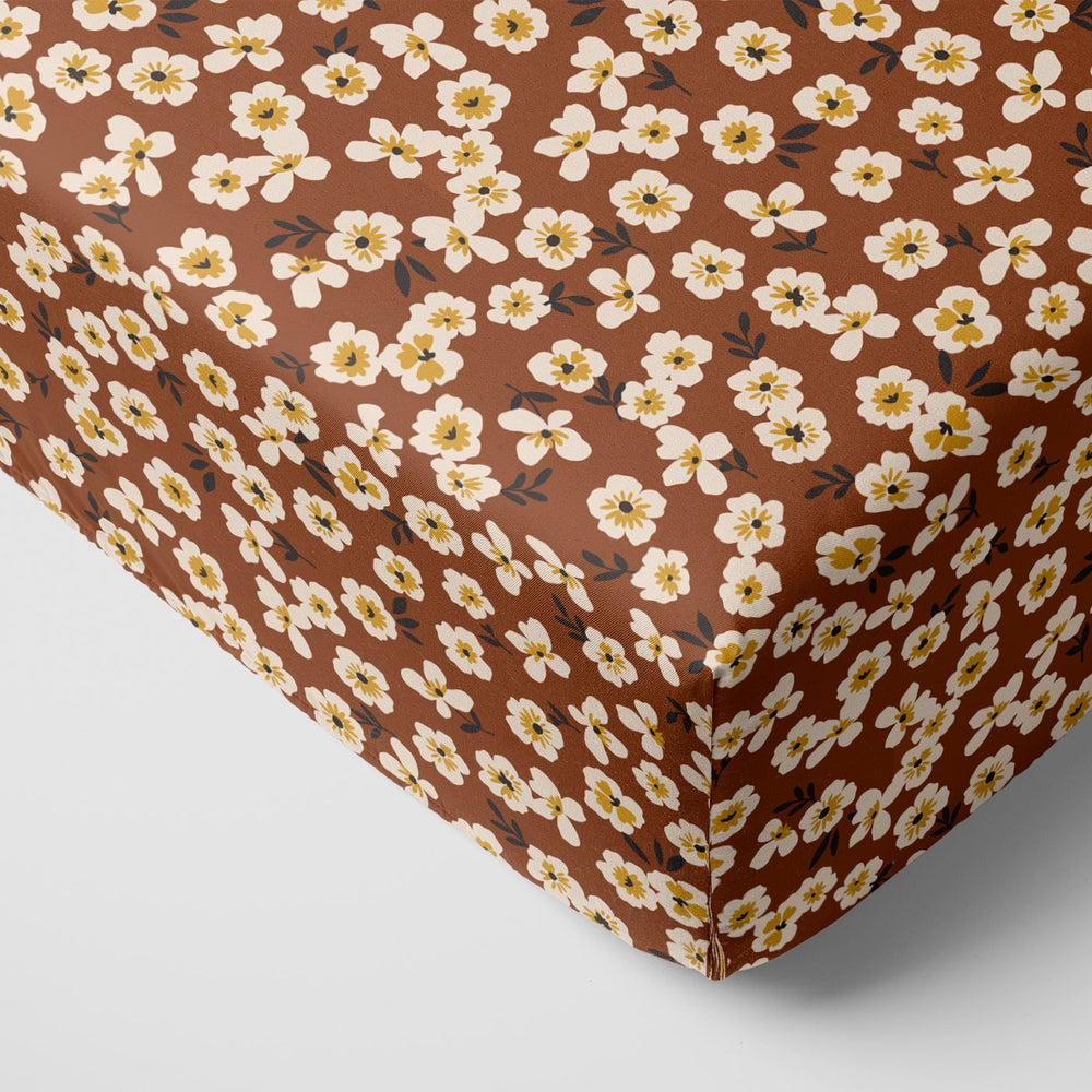 Corner of a mattress with a Mocha Blossom printed fitted crib sheet on