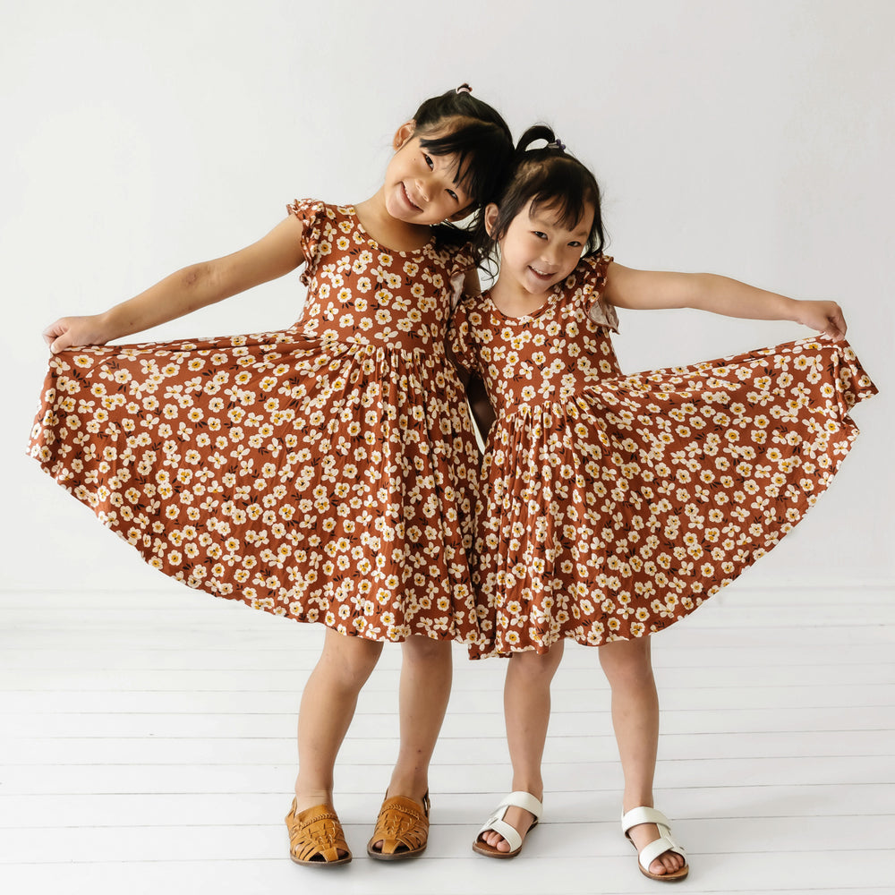 Two children wearing Mocha Blossom printed twirl dresses and holding out the sides