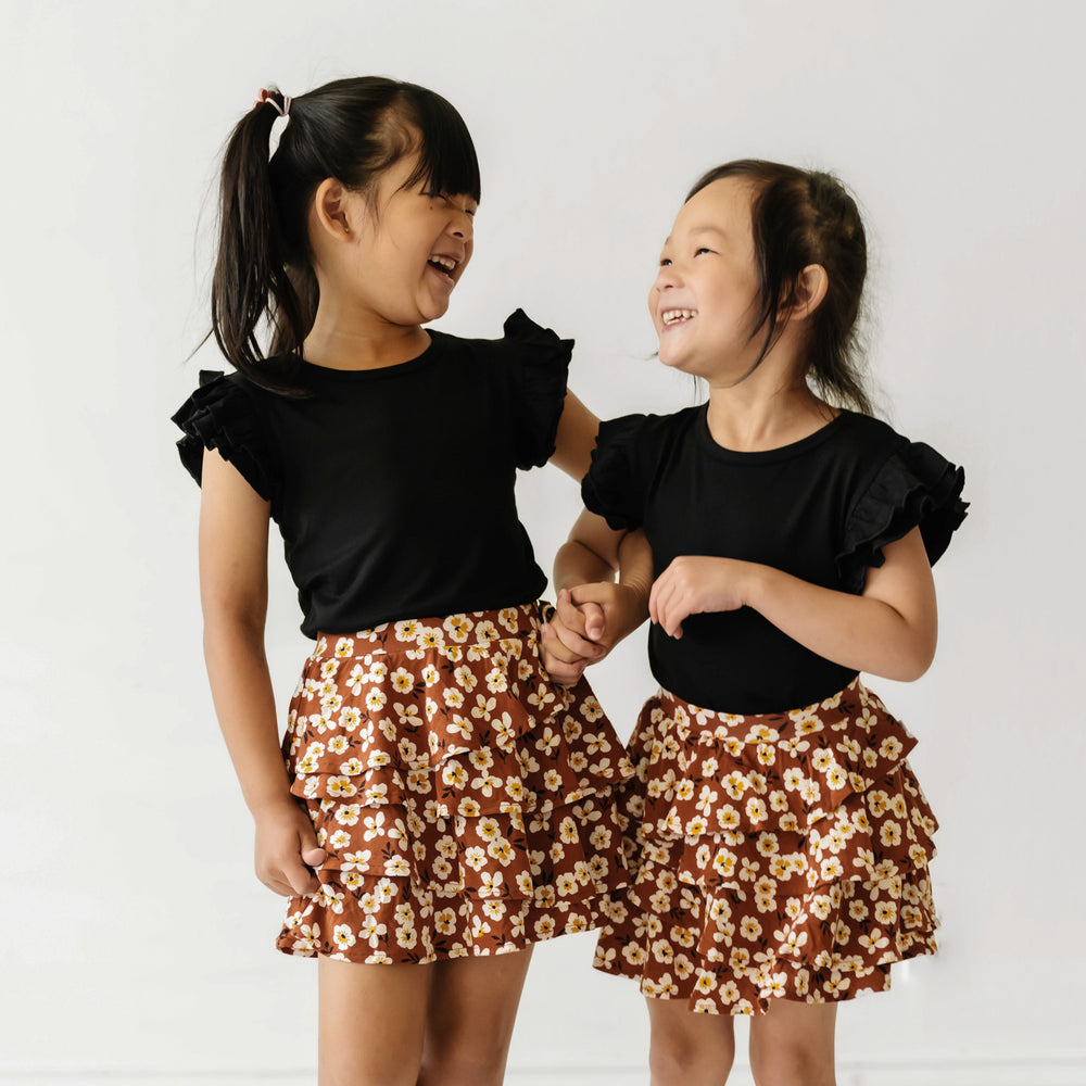 Two children laughing and holding hands wearing matching Mocha Blossom printed ruffle skorts
