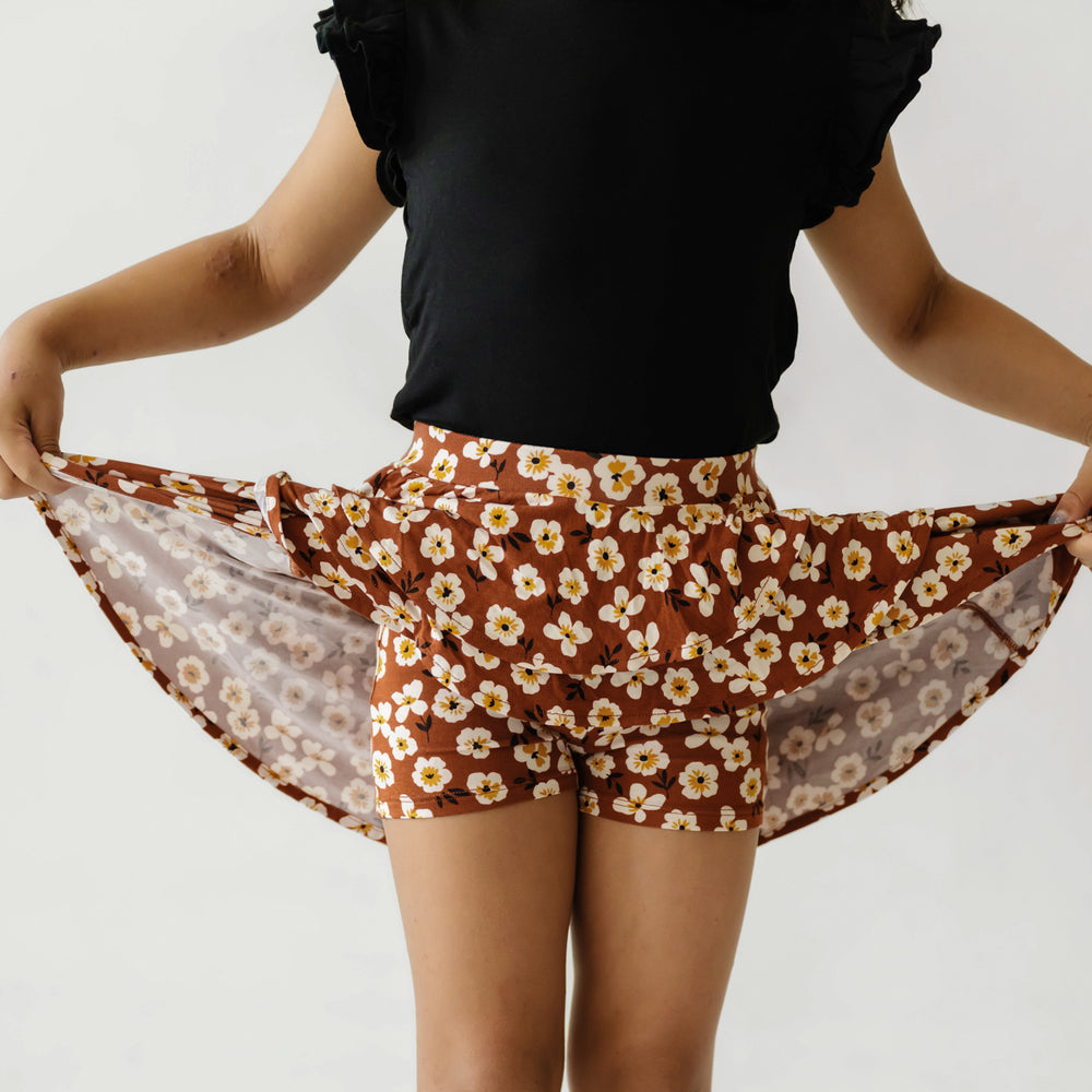 Child wearing a Mocha Blossom printed ruffle skort holding up the skirt to show the shorts underneath