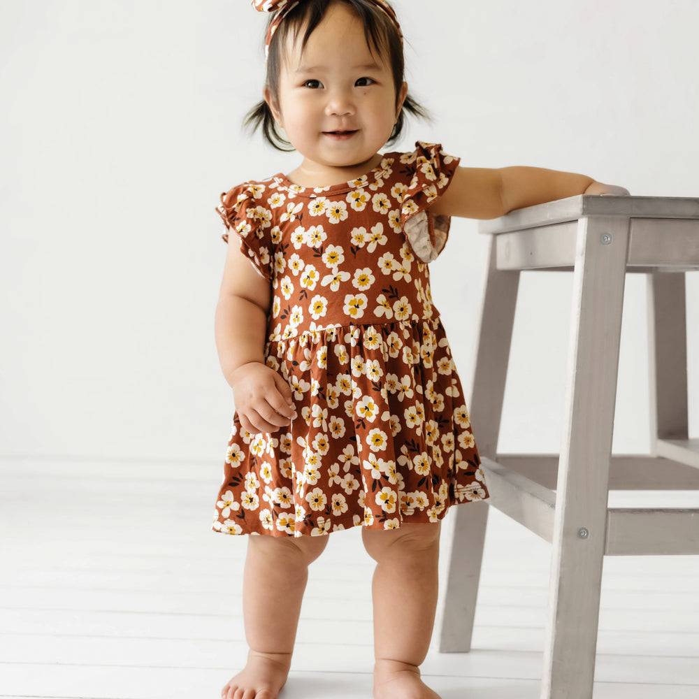 Child standing by a stool wearing a Mocha Blossom printed twirl dress with bodysuit