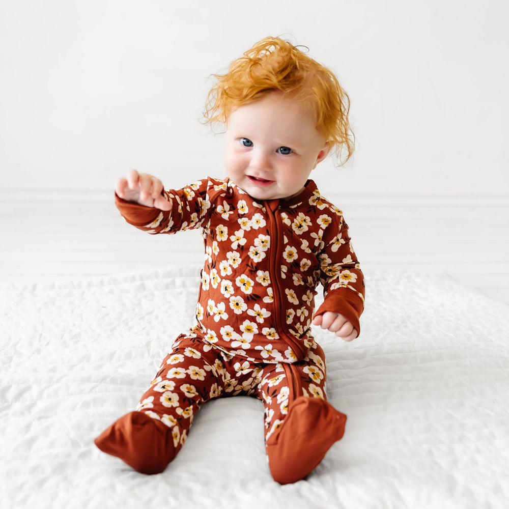Child sitting down on a bed wearing a Mocha Blossom printed zippy