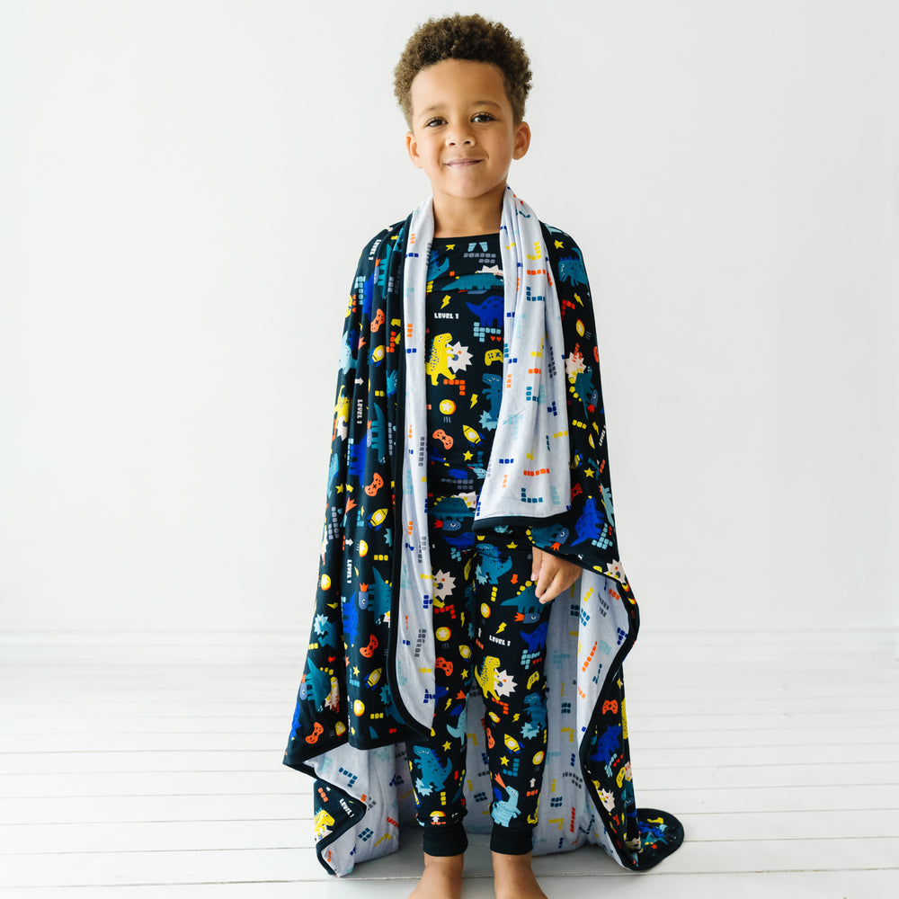Child wearing a Next Level Dinos cloud blanket over his shoulders and matching Next Level Dinos printed two piece pajama set