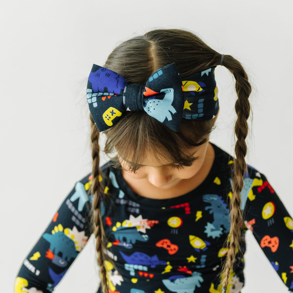Child showing a close up of her Next Level Dinos luxe bow headband paired with matching Next Level Dinos two piece pajama set