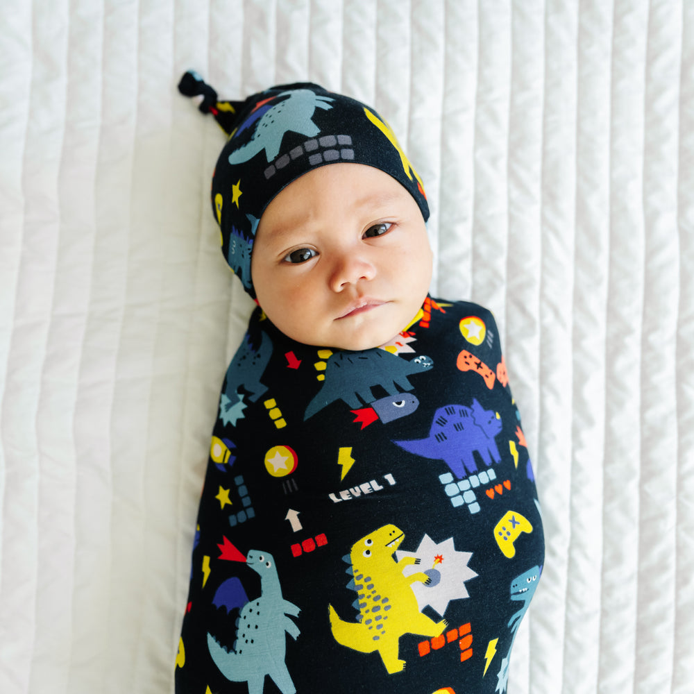 Close up image of a child laying on a bed swaddled in a Next Level Dinos swaddle and hat set