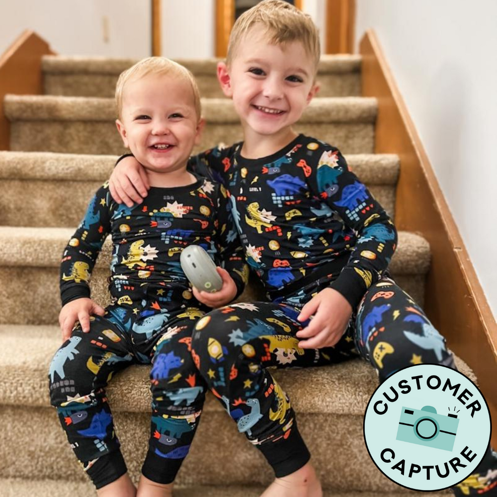 Customer Capture image of two children sitting together wearing matching Next Level Dinos two piece pajama sets