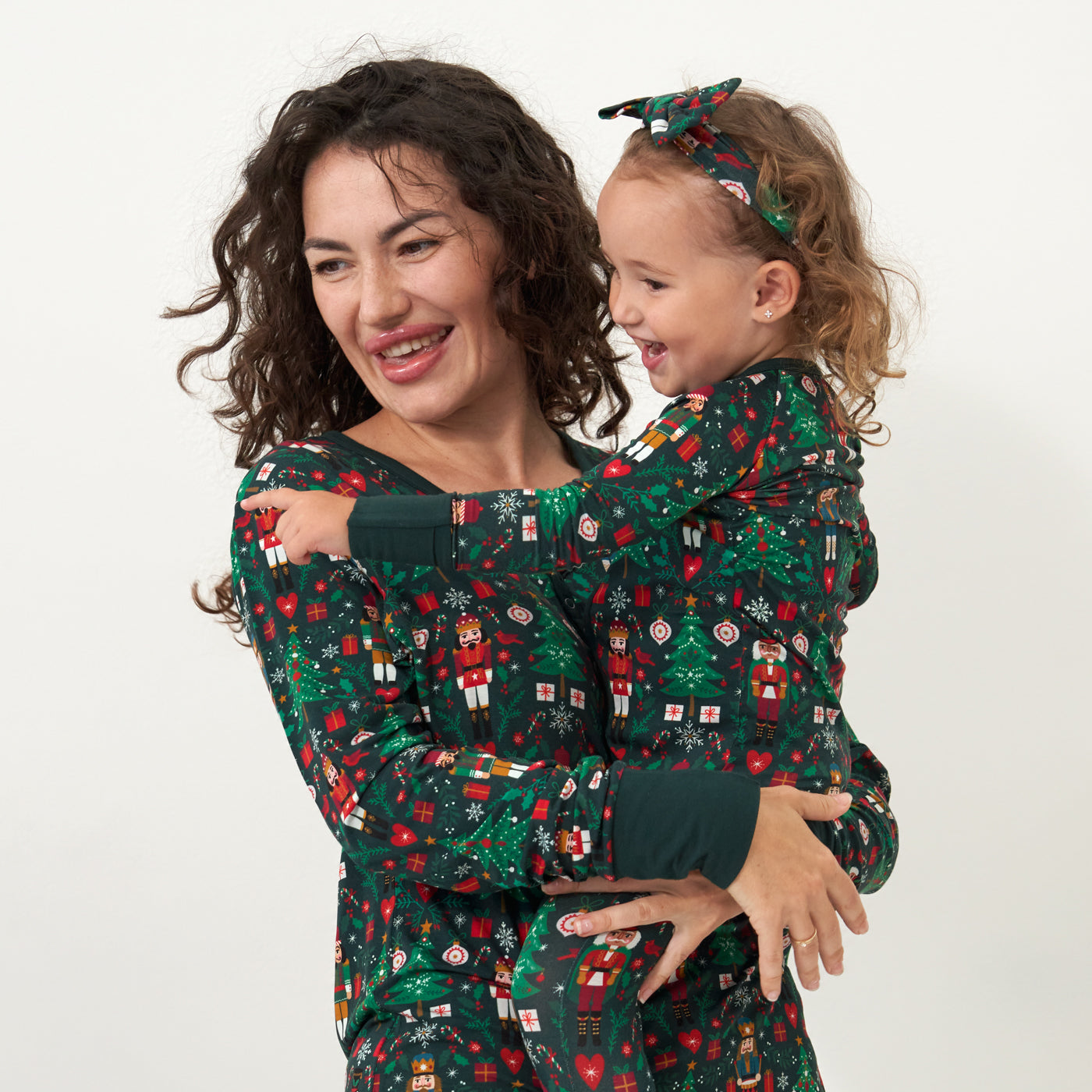 Woman holding her daughter on her hip. Mom is wearing a women's Night at the Nutcracker women's pajama top and her daughter is wearing a Night at the Nutcracker zippy paired with a matching luxe bow headband