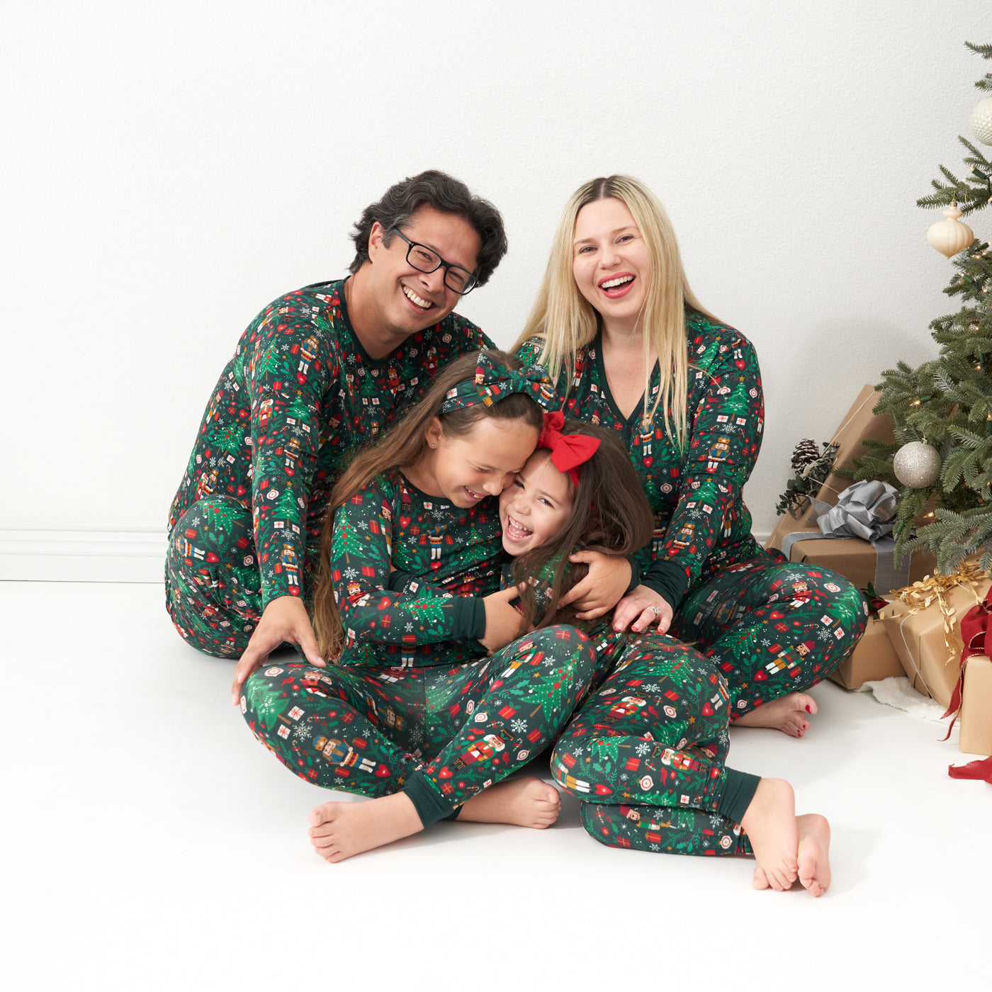 Dad and his two daughter posing wearing Night at the Nutcracker pajama sets. Dad is wearing a Men's Night at the Nutcracker printed men's pajama top and men's pajama bottoms. The older daughter is wearing a two piece Night at the Nutcracker two piece pajama set paired with a matching luxe bow headband. Their youngest child is wearing a Night at the Nutcracker printed zippy paired with a matching luxe bow headband