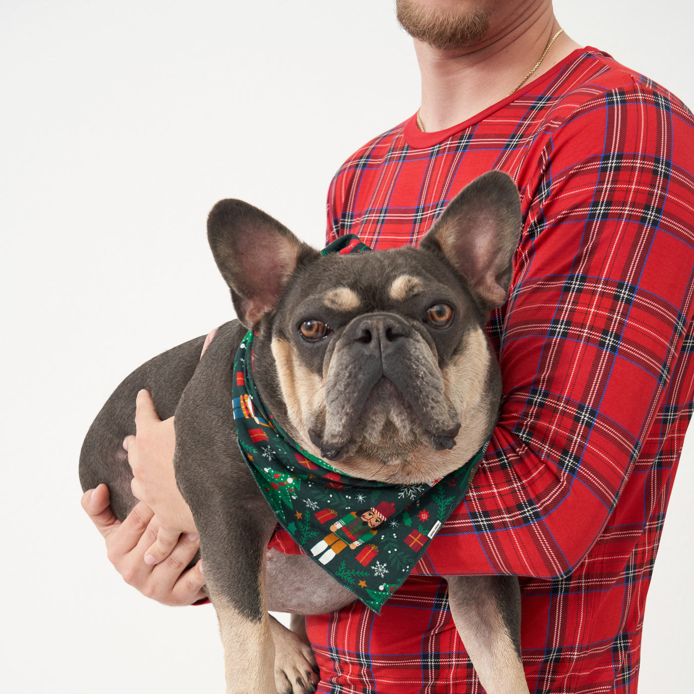 Man wearing a men's Holiday Plaid pajama top holding a dog wearing a Night at the Nutcracker pet bandana 