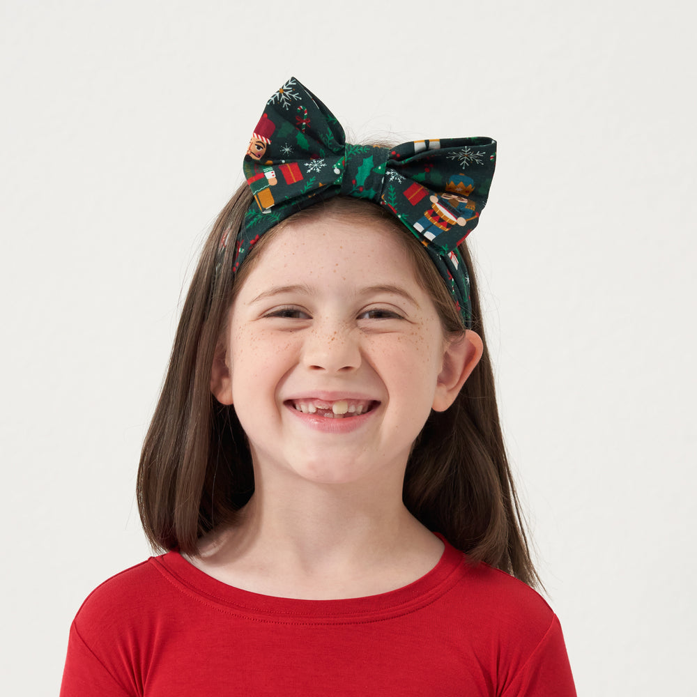 Close up image of a child wearing a Night at the Nutcracker luxe bow headband with a Holiday Red two piece pajama set