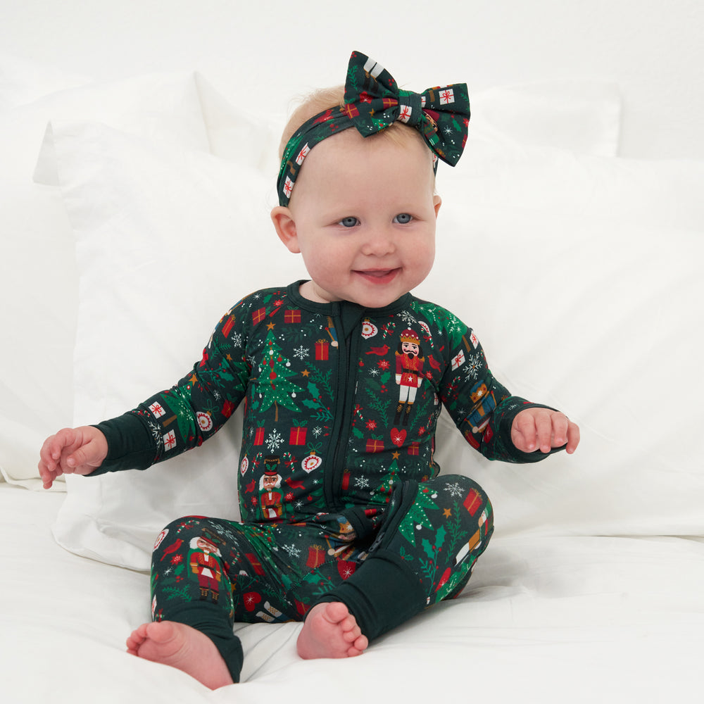 Child sitting on a bed wearing a Night at the Nutcracker zippy paired with a matching luxe bow headband