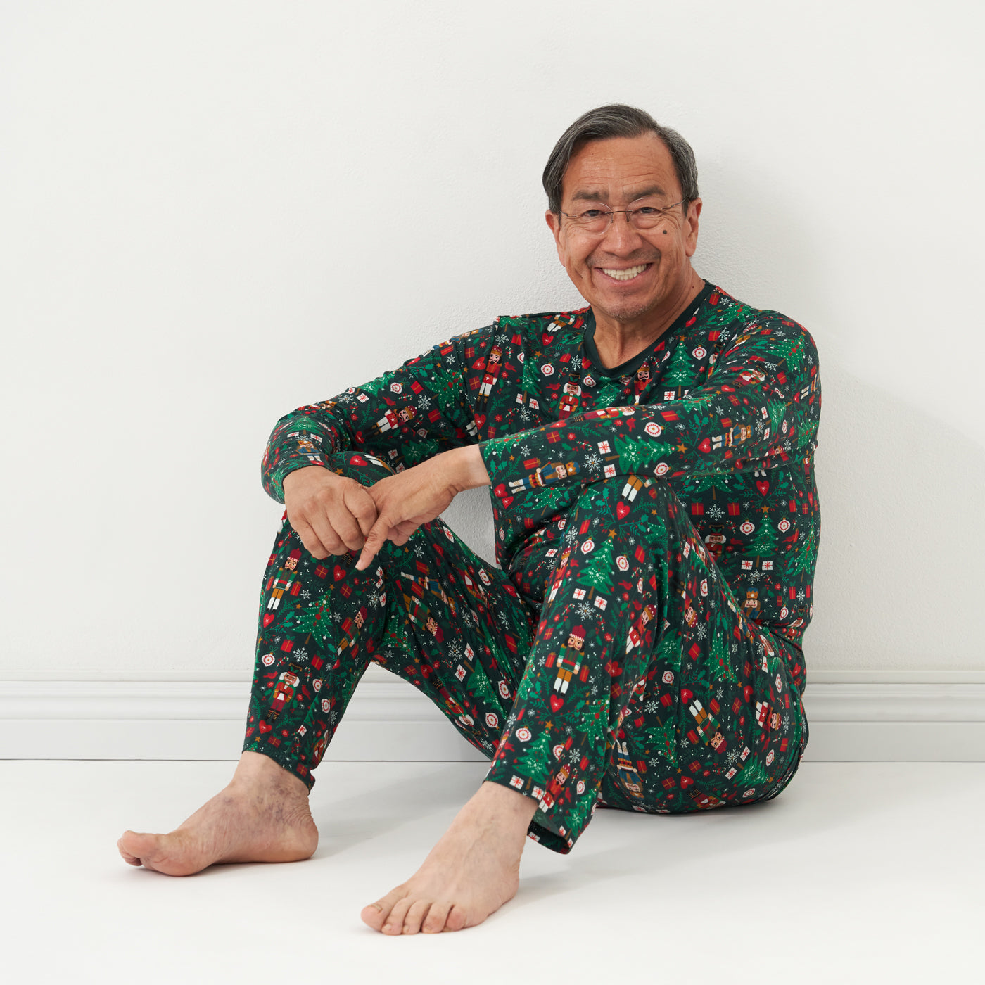 Man sitting wearing men's Night at the Nutcracker pajama top and matching pajama bottoms.