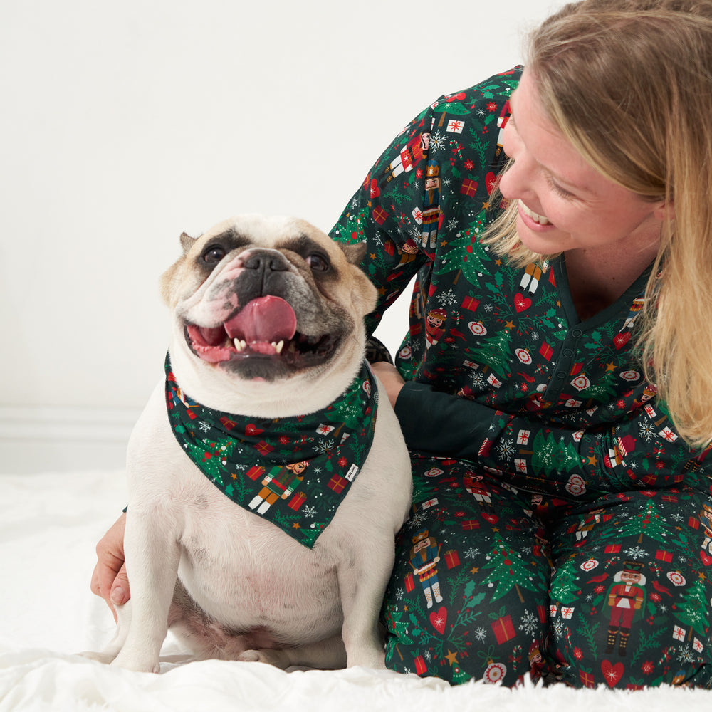 Woman posing with her pet dog. Woman is wearing a Night at the Nutcracker printed women's pajama top and matching women's pajama bottoms. Her dog is wearing a Night at the Nutcracker pet bandana 
