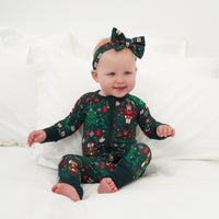 Child sitting on a bed wearing a Night at the Nutcracker zippy paired with a matching luxe bow headband