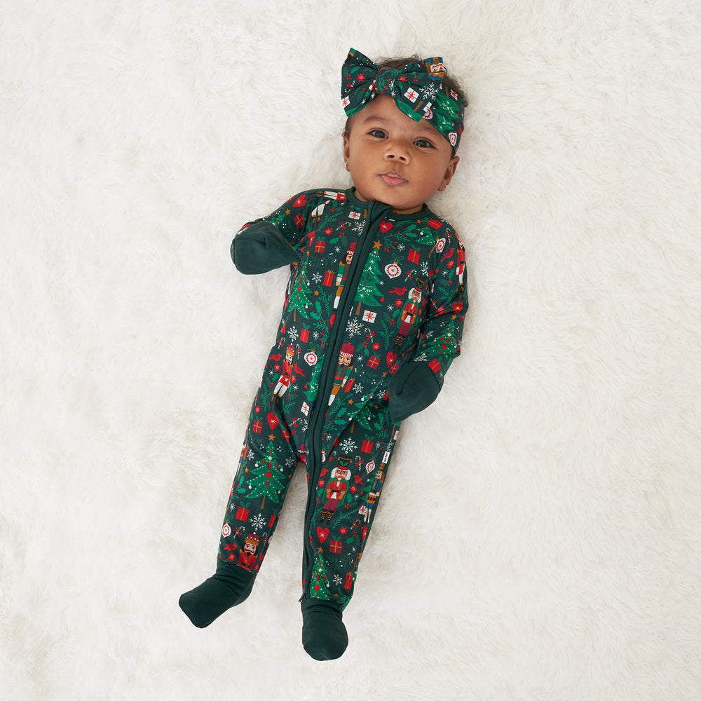Child laying on a blanket wearing a Night at the Nutcracker zippy paired with a matching luxe bow headband. Child is showing the fold over mittens and feet